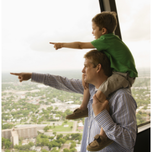 Father with son on shoulders pointing out a window at something in the distance